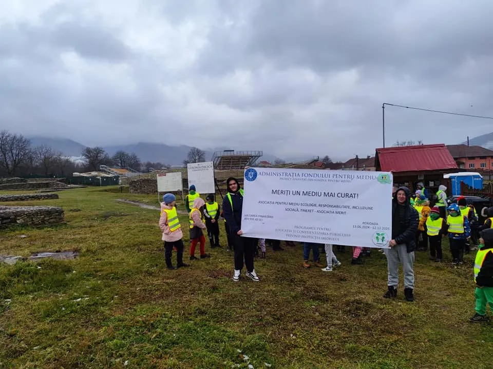 Copii în veste reflectorizante țin bannerul proiectului „Meriți un mediu mai curat!” într-un sit din Țara Hațegului